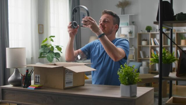 Handsome young man pulls out headphones from a cardboard box. Unpacking online purchases.