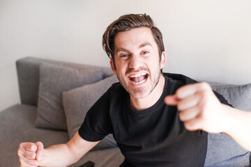 Happy emotional man on a couch screaming, gesticulating with his hands. Concept of watching sport...