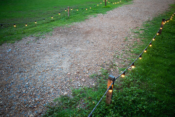 Gravel walking path in a grass field/lawn with light bulb fence