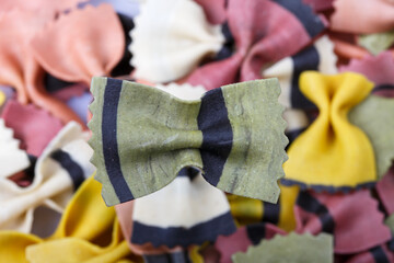 filled frame close up top view flat lay background wallpaper shot of a single green and black raw Italian bow tie farfalle on a bokeh background of scattered colorful multi color pasta
