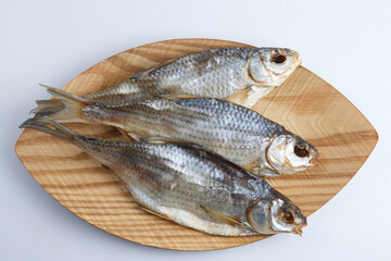 isolated close up top view shot of three Russian dried salted vobla (Caspian Roach) fish on a wooden plate on a white background