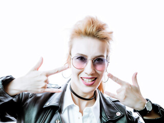 A beautiful girl in a black leather jacket and sunglasses shows hands gesture rock on a bright...