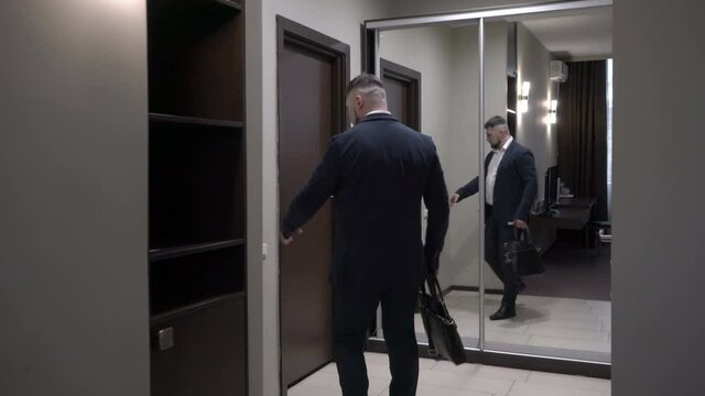Mature businessman leaves a hotel room turning off the light and opens the door.