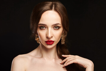 Beautiful young model with red lips and gold earrings on black background