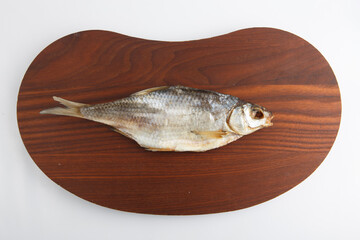 isolated close up top view shot of a single Russian dried salted vobla (Caspian Roach) fish on a dark wooden plate on a white background