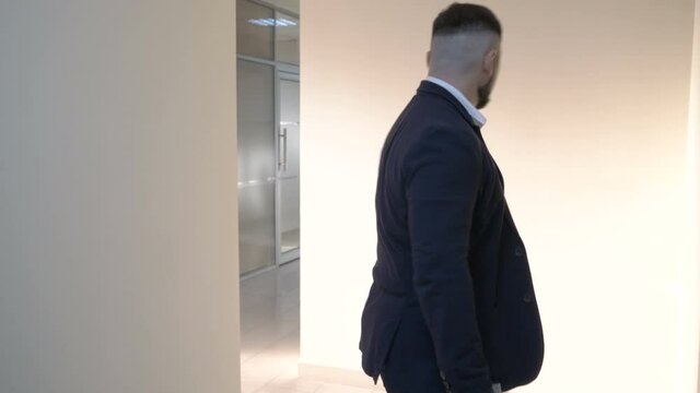 Mature businessman leaves a hotel room turning off the light and opens the door.