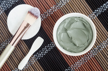 Gray bentonite clay in the bowl, cotton pad and cosmetic brush. Clay texture close up. Diy mask and body wrap recipe. Natural beauty treatment and spa. Top view, copy space