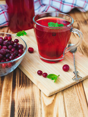 cranberry juice with mint leaves in a glass cup on a bamboo board with a teaspoon on a background of berries and a bottle. Vertical photo, copy space