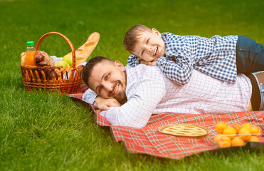 Smiling dad with his little son lying on checkered blanket together during picnic