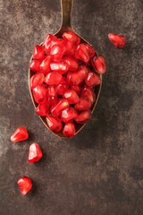 Close up of pomegranate seeds in spoon on dark background. Top view. Close-up