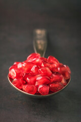 Close up of pomegranate seeds in spoon on dark background. Selective focus. Close-up