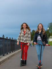 Teenage girls ride scooters in the evening