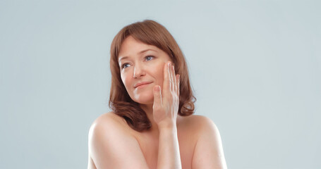 Pretty mature female applies skin care product by touching face with hand. Woman applying anti-age cream on her skin isolated on white background. Spa and wellness concept.