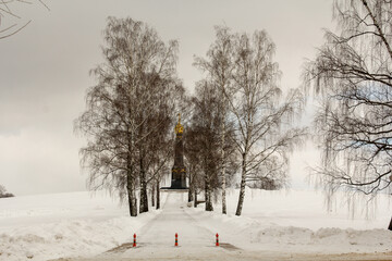 A snowy road past bare birches leading up to a black Church with a Golden dome