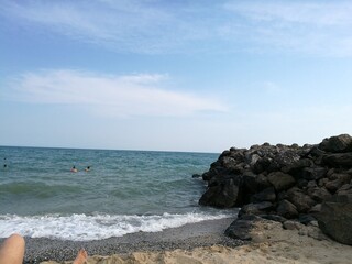 Blue sea waves with white foam rolling on a sandy beach with a black stone breakwater