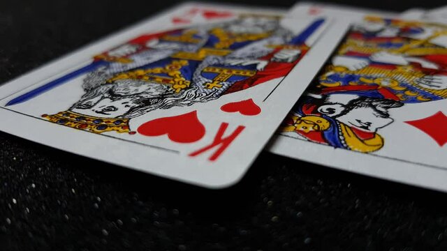 Macro view of kings cards falling on a black shiny table one at a time.
