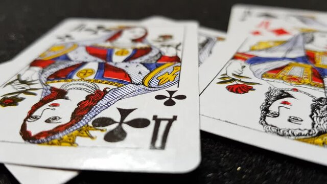 Macro view of cards of queens falling on a black shiny table one by one.