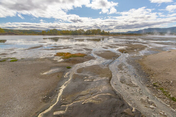 Daytime view in clear sunny weather of the valley of geysers. Mountains and volcanoes are visible on the horizon.