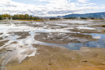Daytime view in clear sunny weather of the valley of geysers. Mountains and volcanoes are visible on the horizon.