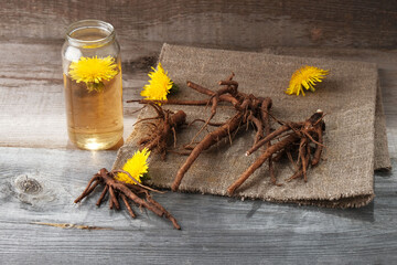 Decoction of flowers and dandelion roots in a glass jar on a vintage wooden background with copy space, medicinal herbs, herbal medicine, traditional medicine, natural cosmetics, herbalism concept
