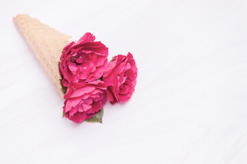 Flowers red roses in a waffle cone on white wooden background. Flat lay, top view, floral background, toned.