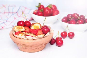 Mini tiny pancakes with straeberries and cherries on white wooden background. Trendy food concept.