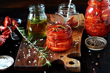 Homemade dried tomatoes in glass jars on a dark background, still life