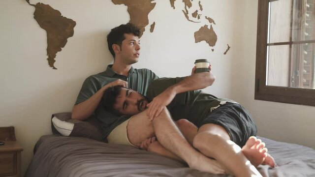 Gay boy couple lying in bed hugging each other. Boy drinks coffee. LGBT