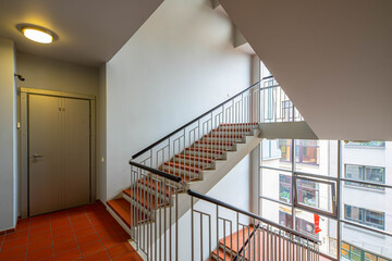 Modern entrance interior in living complex. Flat door. Windows wall. Red tile. Stairs.