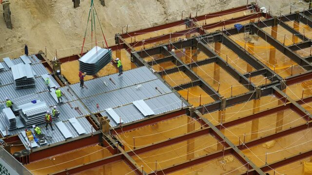 Workers put form sheets for concrete floor filling, time lapse shot of modern building construction site. Crane lift down pack of molds, engineers hand set on place, weld to steel basement frame