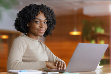 Smiling black lady using laptop at cafe