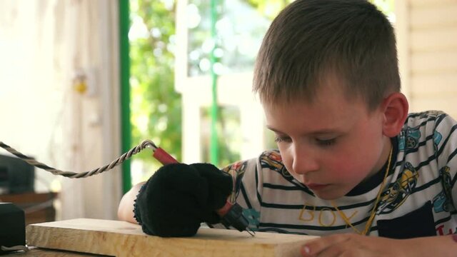 A very diligent 5-7 year-old Caucasian boy is interested in painting on a wooden board. DIY souvenir. Burning drawing on a wooden board