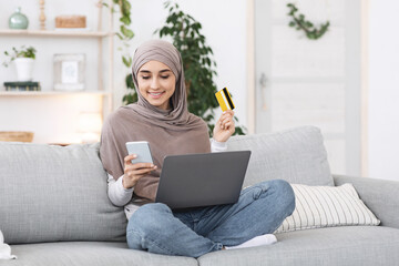 Online Payments. Happy arabic girl using smartphone, laptop and card at home