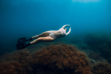 Sporty woman freediver with fins glides underwater in blue sea.