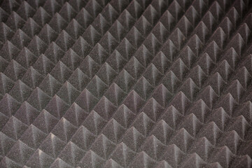 Dark grey diamond-shaped soundproof panel with sharp pyramidal elements. Abstract geometric texture or background.