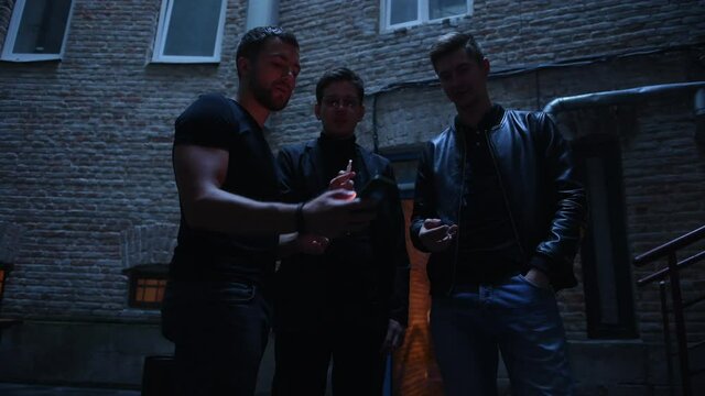 Three male friends stands outside the bar. Having conversation. In nice clothes.