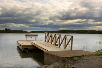 wooden pier with a railing and a bench for relaxing on the lake under a cloudy sky