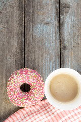 Fototapeta na wymiar A pink doughnut on a wooden planks background with a cup of coffee with milk and a napkin on a vintage wood background with copy space.