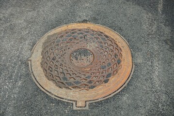 one brown rusty iron sewer manhole lies on the gray asphalt of the road