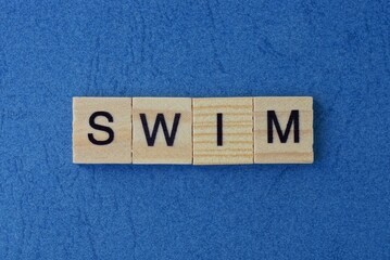 text on gray word swim in small wooden letters with black font on a blue background