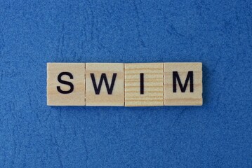 text on gray word swim in small wooden letters with black font on a blue background