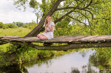 Young charming girl sits on an old wooden bridge with a bouquet of daisies	
