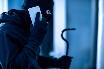 Villain holding crowbar and smartphone preparing burglary