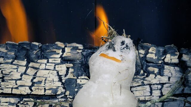 A brave snowman. Little snowman melts in hot stove against background of firewood.
