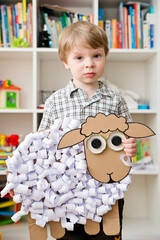 The boy holding hands a paper sheep. DIY toy. Activity at home. Early education, fine motor skills. Montessori methodology.