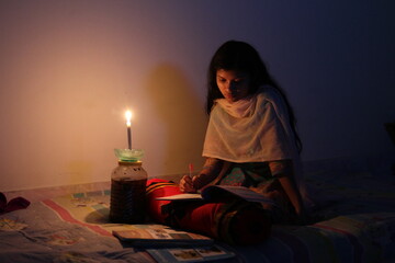 A young girl studying at home with candlelight after electricity load shedding at Dhaka City,...