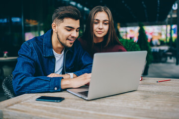 Positive male and female students watching movie on modern laptop computer spending time...