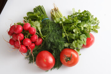 close up top view shot of a vegetable composition consisting of a bunch of radish, dill, parsley, green onions and ripe red tomatoes on a white background