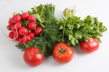 close up top view shot of a vegetable composition consisting of a bunch of radish, dill, parsley, green onions and ripe red tomatoes on a white background
