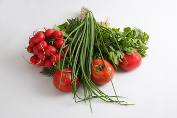 close up top view shot of a vegetable composition consisting of a bunch of radish, dill, parsley, green onions and ripe red tomatoes on a white background